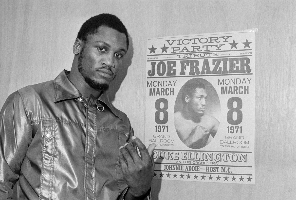 ARCHIV: Heavyweight champ Joe Frazier poses by a poster advertising his "victory party" as he leaves his dressing room after a final public workout in Philadelphia before his title defense b ...