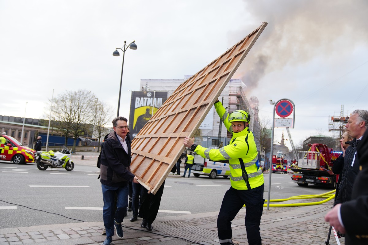 epa11281327 Locals carry paintings and other objects as a fire burns the old Stock Exchange (Boersen) in Copenhagen, Denmark, 16 April 2024. A violent fire broke out in the building which is under ren ...