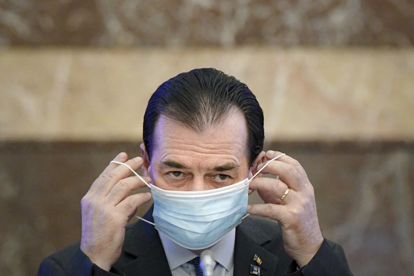 FILE - In this May 14, 2020 file picture Romanian Prime Minister Ludovic Orban handles his face mask before attending a meeting ahead of the loosening of measures taken by the government to combat the ...
