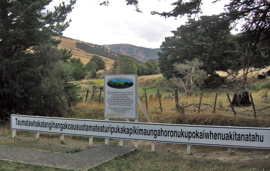 Langer Ortsname auf Neuseeland: Taumatawhakatangihangakoauauotamateaturipukakapikimaungahoronukupokaiwhenuakitanatahu
Schild mit Namen, Berg im Hintergrund