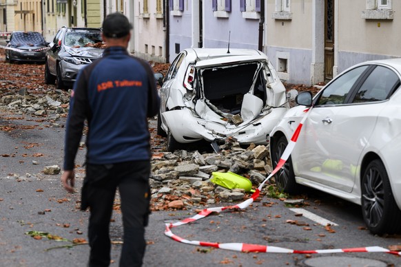 Une personne marche entre les voitures endommagees par la chute des tuiles d&#039;un toit, un jour apres la forte tempete le mardi 25 juillet 2023 a La Chaux-de-Fonds. Le deblaiement des materiaux et  ...