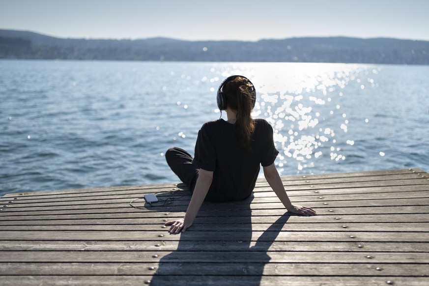 Eine Frau sitzt mit Kopfhoerern auf einem Steg am See, fotografiert am 24. Juni 2020 in Zuerich. (KEYSTONE/Gaetan Bally)