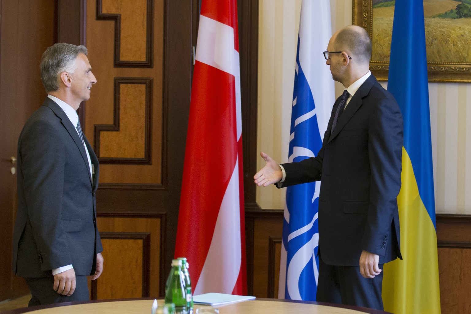 Es ist tatsächlich nicht die Schweizerfahne, die da neben der OSZE- und der ukrainischen Fahne hängt: Der Chef der Übergangsregierung in Kiew, Arsenij Jazenjuk (r.), scheint während der Handshake-Zere ...