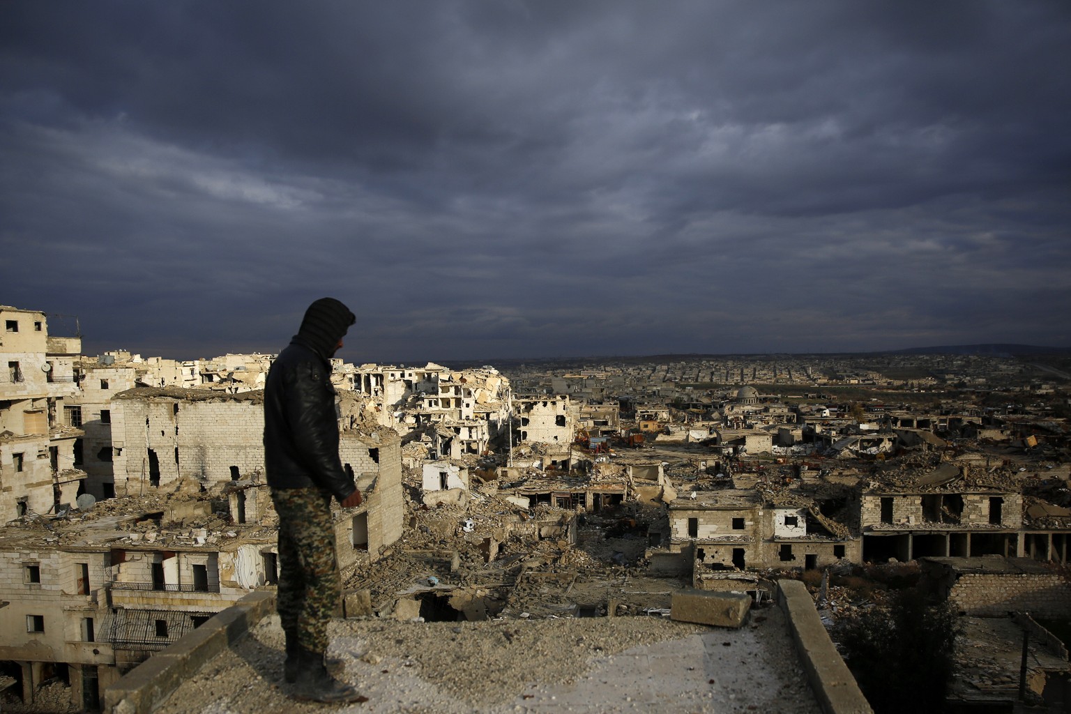 In this Jan. 19, 2018 photo, a soldier looks at the destruction of the Ramouseh neighborhood from a the roof of a damage, in eastern Aleppo, Syria. The government has started its first organized recon ...