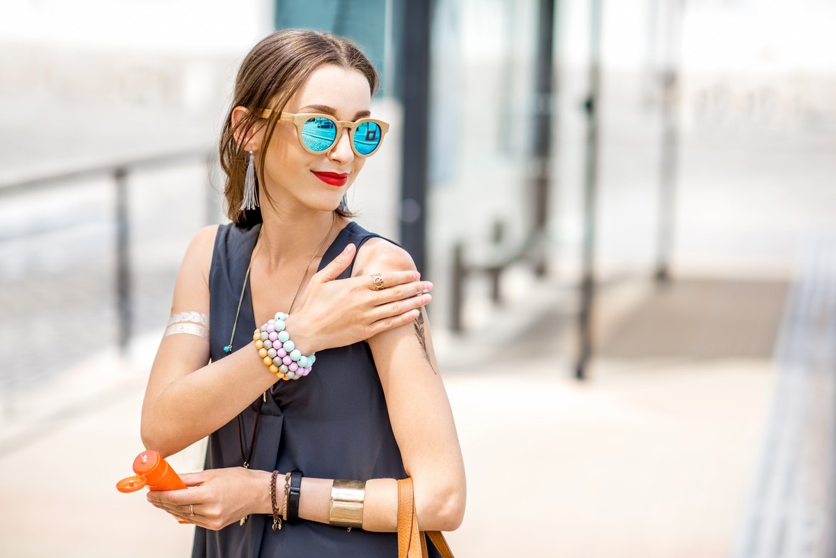 Young woman applying sunscreen lotion standing outdoors at the urban location during the sunny weather