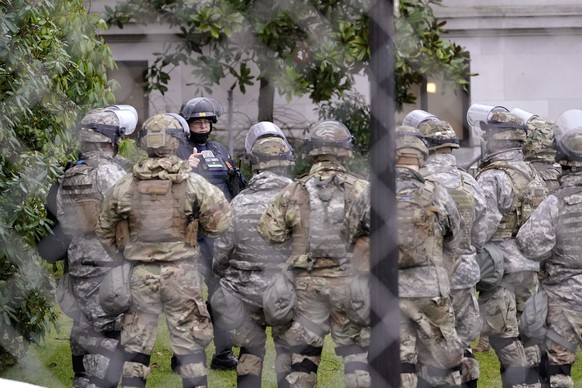 A Washington State Patrol trooper talks with members of the Washington National Guard inside a fence surrounding the Capitol in anticipation of protests Monday, Jan. 11, 2021, in Olympia, Wash. State  ...
