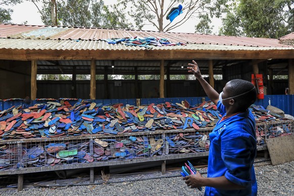 epa10228965 A Kenyan worker from the social enterprise &#039;Ocean sole&#039; throws old flip-flops onto a roof for drying them as preparation for further processing them at their workshop in Nairobi, ...