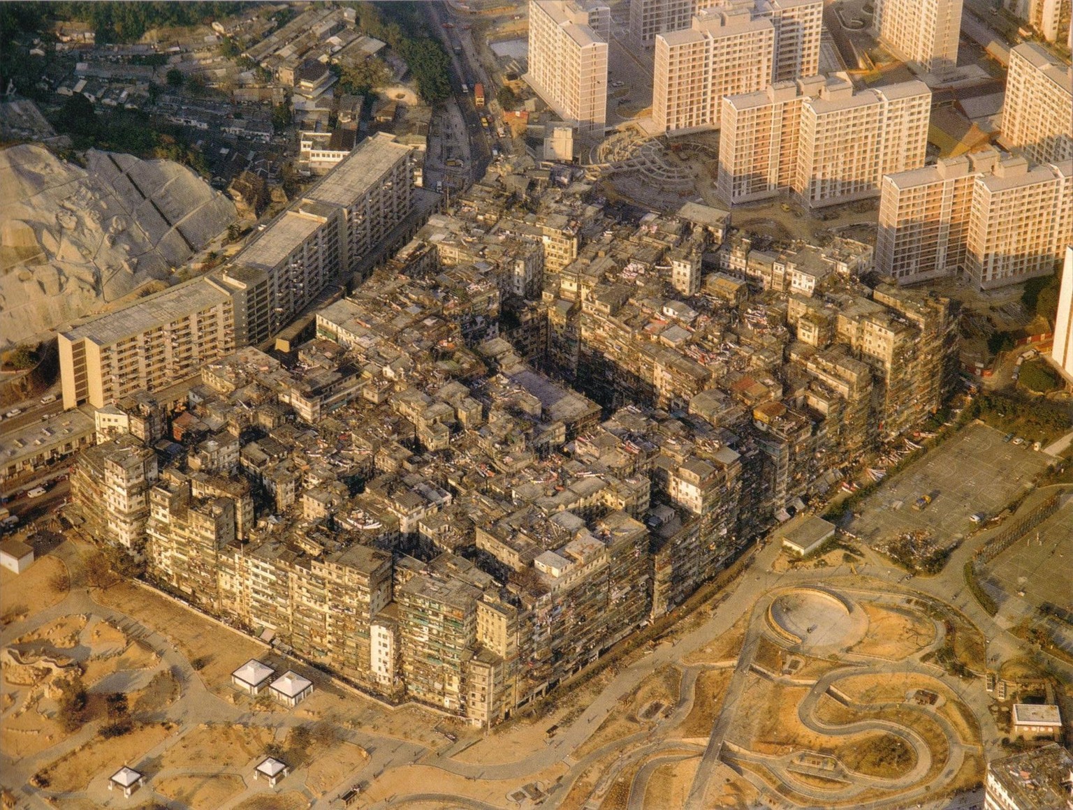 Ein Luftbild der Kowloon Walled City aus dem Jahr 1989. Am Südrand der Stadt ist der neue Park zu sehen, der an der Stelle der ehemaligen Squatter-Siedlung Sai Tau Tsuen angelegt wurde.