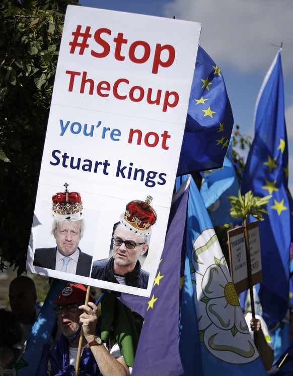 A protester holds a banner with images of Dominic Cummings, right, political strategist and special advisor to British Prime Minister Boris Johnson, left, as they protest outside the Houses of Parliam ...