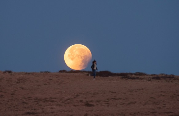 epa09950414 A woman runs in front the Moon during an eclipse in the village of Tindaya, Fuerteventura island, southwestern Spain, early 16 May 2022. EPA/Carlos de Saa