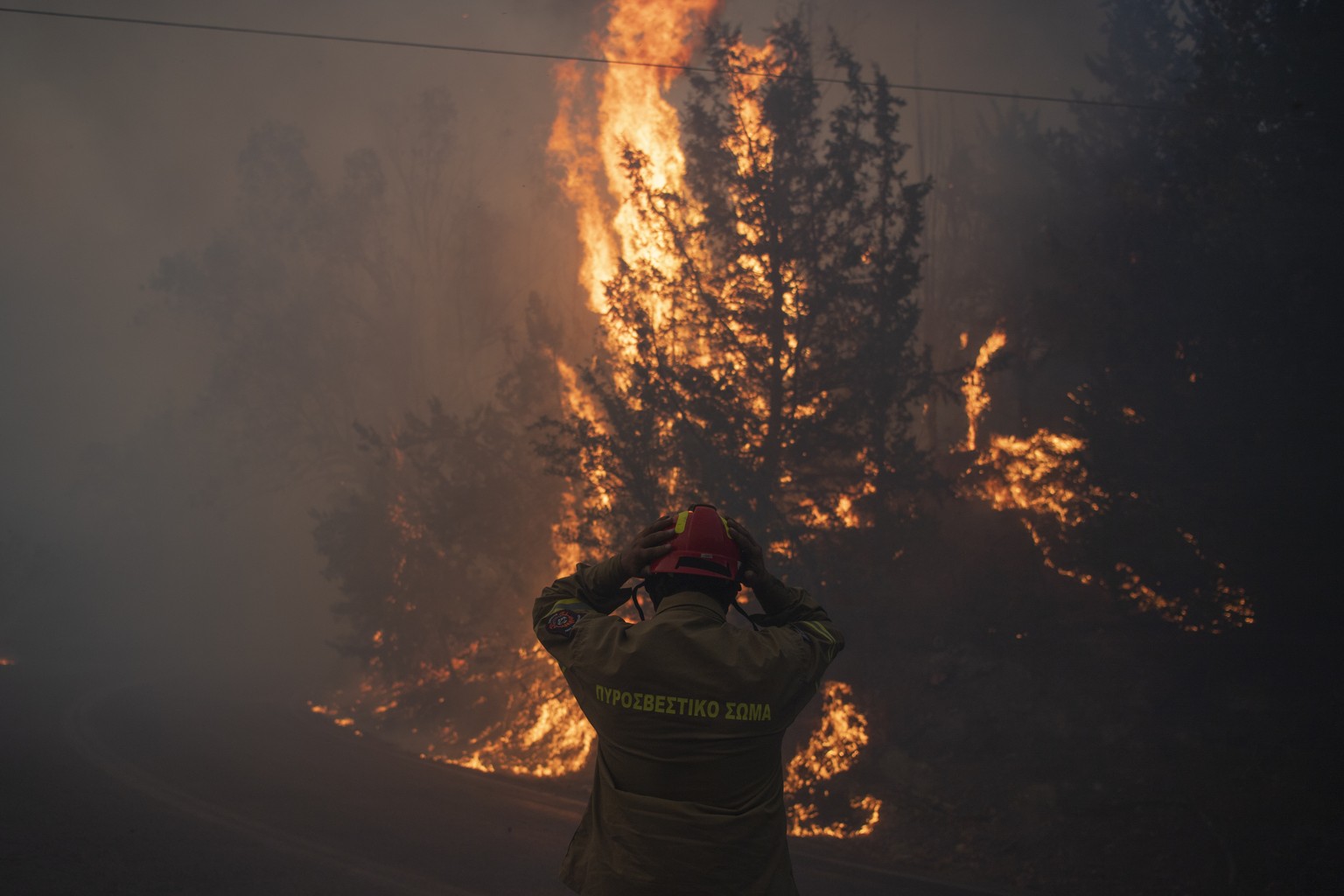 A firefighter adjusts his helmet in Varnava village during a wildfire, north of Athens, Greece, Sunday, Aug. 11, 2024, with many regions of the country on high alert due to high temperatures and wind  ...
