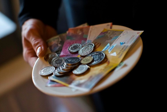 A waitress presents a plate with various Swiss Franc coins and notes in this picture illustration in a restaurant in Zurich, Switzerland, May 21, 2013. REUTERS/Michael Buholzer/Illustration/File Photo