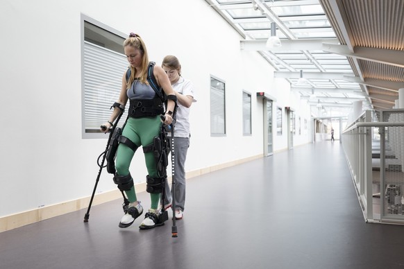 Ein Patientin des Schweizer Paraplegiker-Zentrums geht mit dem Exoskelett und einer Therapeutin durch den Gang, aufgenommen am Dienstag, 26. Februar 2024 in Nottwil. Mit dem Exoskelett koennen Betroff ...