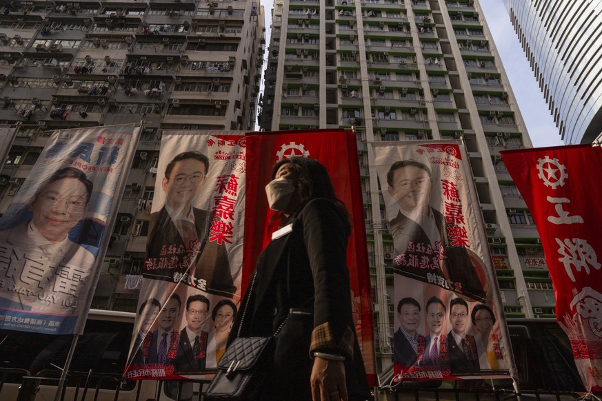 A pedestrian walks past banners promoting candidates for upcoming district council elections in Hong Kong, Monday, Dec. 4, 2023. (AP Photo/Louise Delmotte)