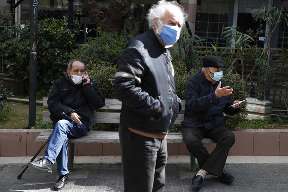 Two elderly men sit on a bench as another one waits in a queue to conduct a rapid test for the COVID-19 in Athens, Wednesday, March 3, 2021. Greece has recorded a new spike in COVID-19 infections, nea ...