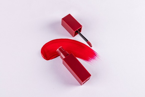 Eine offene Verpackung mit einem Balsam Pinsel oder Lippenstift liegt auf der kosmetischen Abstrich des Produkts. rote Textur. Ansicht von oben. Eine leere Produktverpackung Mockup. An open package wi ...