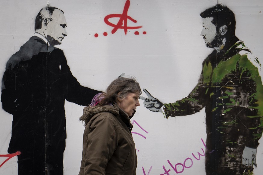 A woman walks by a graffiti depicting Ukrainian President Volodymyr Zelenskyy, right, and Russian President Vladimir Putin in central London, Thursday, May 4, 2023. (AP Photo/Vadim Ghirda)