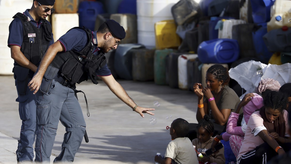 A police officer plays with a migrant child blowing soap bubbles in the port of the Sicilian island of Lampedusa, southern Italy, Monday, Sept. 18, 2023. The Italian Cabinet met Monday to adopt new me ...