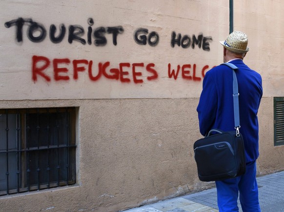 A man looks a grafitti reads Tourist go home. Refugees welcome in downtown, Palma Majorca, Balearics Islands, Spain on 13 April 2016. Some grafittis have appeared in the central streets of the city ag ...