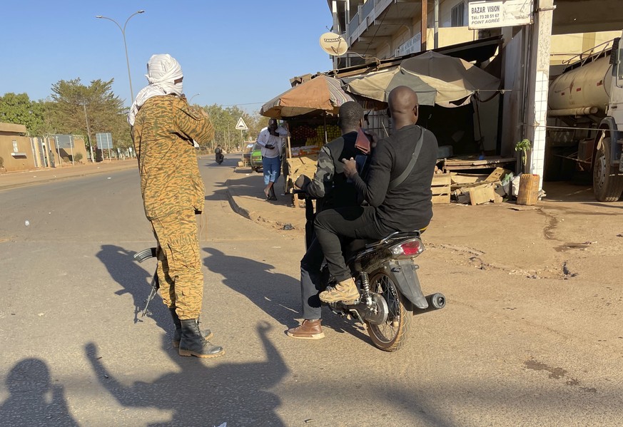 Two men ride past a military checkpoint outside a military base in Burkina Faso&#039;s capital Ouagadougou Sunday Jan. 23, 2022. Witnesses are reporting heavy gunfire at a military base raising fears  ...