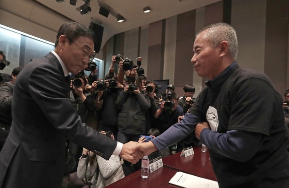 Hwang Sang-gi, right, father of former Samsung semiconductor factory worker Hwang Yu-mi who died from leukemia in 2007, shakes hands with Kinam Kim, left, President &amp; CEO of Samsung Electronics De ...