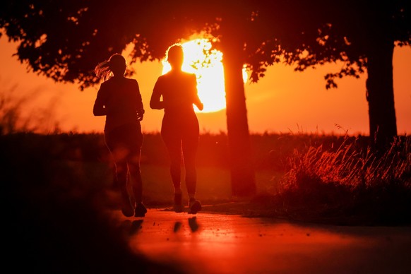 ARCHIV - 22.06.2025, Baden-W�rttemberg, Uttenweiler: Zwei Frauen joggen am Morgen, w�hrend hinter ihnen die Sonne auf geht (zu dpa: �Sturm und Sonne: Wetterumschwung mit sommerlichen Aussichten�) Foto ...