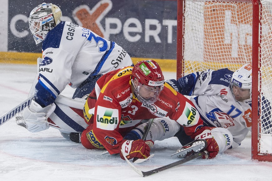 Biels Mike Kuenzle, Mitte, im Duell mit Zuerichs Torhueter Lukas Flueeler, links, und Zuerichs John Quenneville im Eishockey Meisterschaftsspiel der National League zwischen dem EHC Biel und den ZSC L ...