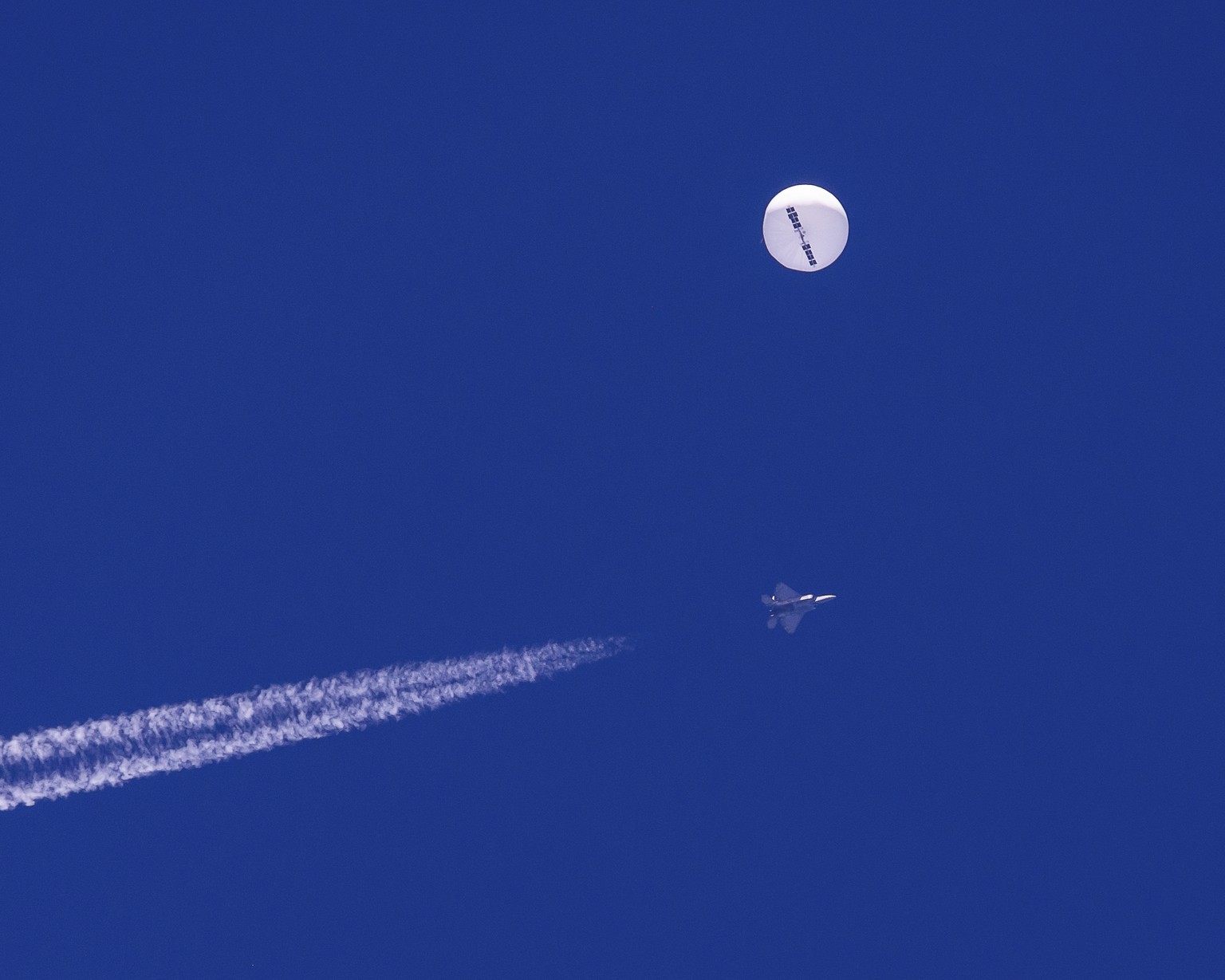 In this photo provided by Chad Fish, a large balloon drifts above the Atlantic Ocean, just off the coast of South Carolina, with a fighter jet and its contrail seen below it, Saturday, Feb. 4, 2023. T ...