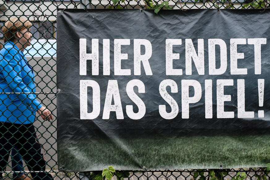 epa06804238 German Chancellor Angela Merkel passes-by a poster reading: &#039;Here the game ends!&#039;, after a visit to the sports club &#039;SV Rot-Weiss Viktoria Mitte 08&#039;, in Berlin, Germany ...