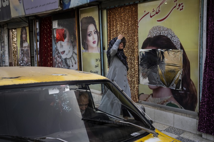 A woman walks past beauty salons with window decorations which have been defaced in Kabul, Afghanistan, Sunday, Sept. 12, 2021. Since the Taliban gained control of Kabul, several images depicting wome ...