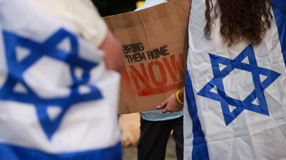 epa11534259 A participant (R) with an Israeli flag hanging from her body holds a cardboard reading &#039;Bring them home now&#039; during a vigil against anti-Semitism in Berlin, Germany, 07 August 20 ...