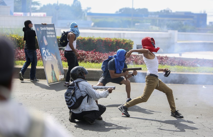 Masked protesters fire from a homemade mortars at riot police as another winds up to throw a rock during a third day of violent clashes in Managua, Nicaragua, Friday, April 20, 2018. The clashes, pitt ...