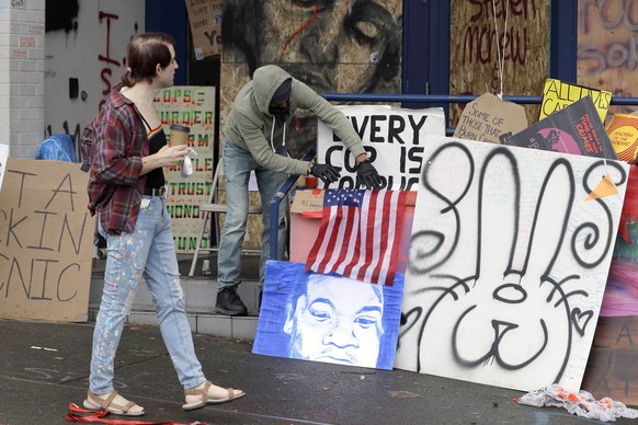 A pedestrian looks on as a person adjusts a U.S. flag displayed on the steps of the Seattle Police East Precinct building, Saturday, June 20, 2020, inside what has been named the Capitol Hill Occupied ...