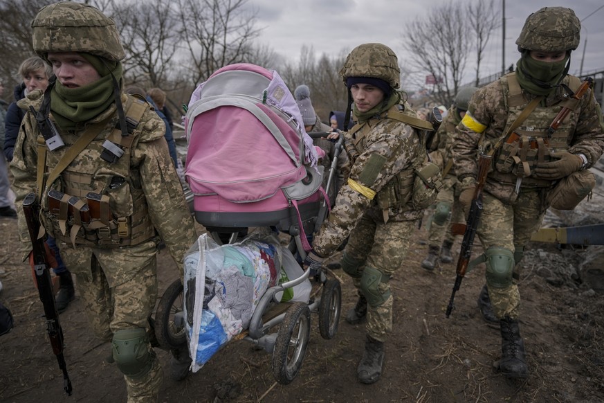 Ukrainian servicemen carry a baby stroller after crossing the Irpin river on an improvised path under a bridge that was destroyed by a Russian airstrike, while assisting people fleeing the town of Irp ...
