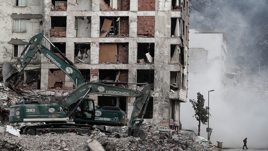 epaselect epa10499211 A man walks through a cloud of dust as a demolition team demolishes a damaged building following a powerful earthquake in Hatay, Turkey, 02 March 2023. More than 50,000 people di ...