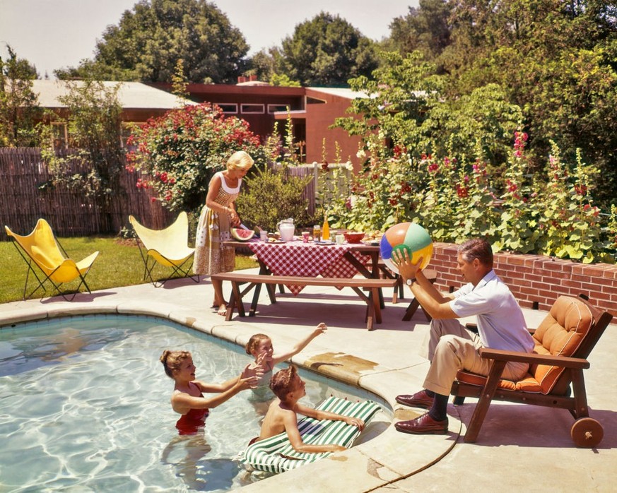 1950s 1960s FAMILY AROUND BACKYARD SWIMMING POOL MOTHER AT PICNIC TABLE FATHER PLAYING BALL WITH KIDS IN POOL (Photo by H. Armstrong Roberts/ClassicStock/Getty Images)