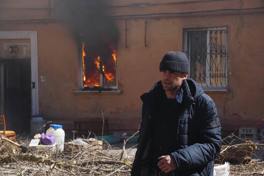 Ein Mann steht vor einem brennenden Haus in Mariupol.