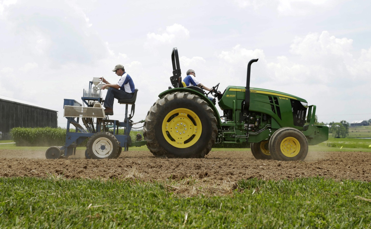 Richard Mundell, left, sits on a plot seeder pulled by a tractor driven by Mark Sizemore, as they plant hemp seeds at the UK Spindletop Research Farm off of Newtown Pike in Lexington, Ky., on Tuesday, ...