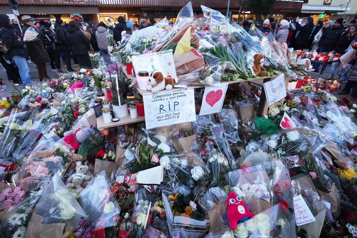 FILE - People stand around floral tributes and candles placed outside the sealed off Le Constellation bar in Crans-Montana, Swiss Alps, Switzerland, on Jan. 3, 2026, where a devastating fire left dead ...