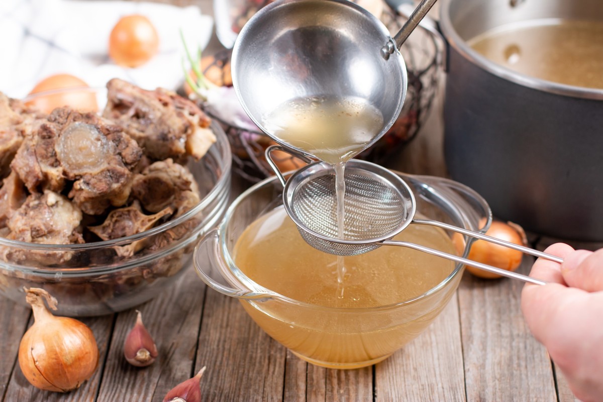 Saucepan mit Bouillon mit einer Leiter auf dem Tisch. Knochenbrühe