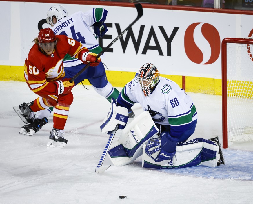 Vancouver Canucks goalie Collin Delia, right, keeps his eyes on the puck as defenseman Travis Dermott, center, checks Calgary Flames center Cody Eakin during the second period of a preseason NHL hocke ...