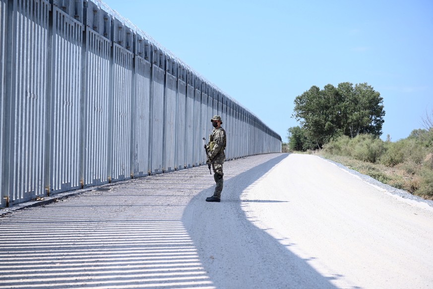 epa09440117 A soldier stands in front of a steel fence built along the Evros River in the area of Feres, at the Greek-Turkish border, Greece, 01 September 2021. The fence was built to prevent the ille ...