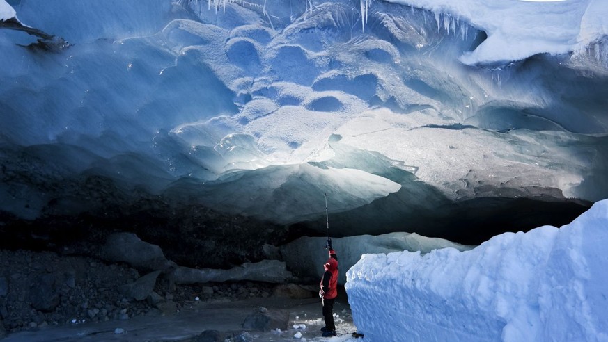 ADVENTSKALENDER 2013 - BILD 2 VON 24 BILDERN –Ein Besucher betrachtet am Sonntag, 3. Januar 2010, das riesige Ausmass der natuerlichen Eisgrotte an der Zunge des Morteratschgletscher bei Pontresina im ...