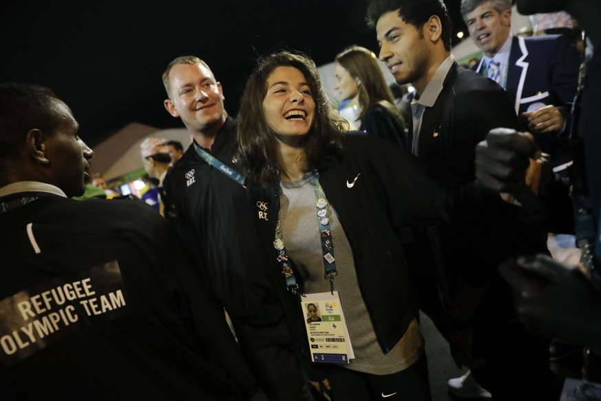Refugee Olympic Team's Yusra Mardini, center, smiles during a welcome ceremony held at the Olympic village ahead of the 2016 Summer Olympics in Rio de Janeiro, Brazil, Wednesday, Aug. 3, 2016. (AP Pho ...