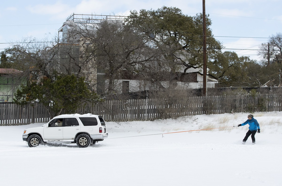 Ehsan M. rides a snowboard behind a friend's SUV in a parking lot in Travis Heights after a heavy snow on Monday Feb. 15, 2021. (Jay Janner /Austin American-Statesman via AP)