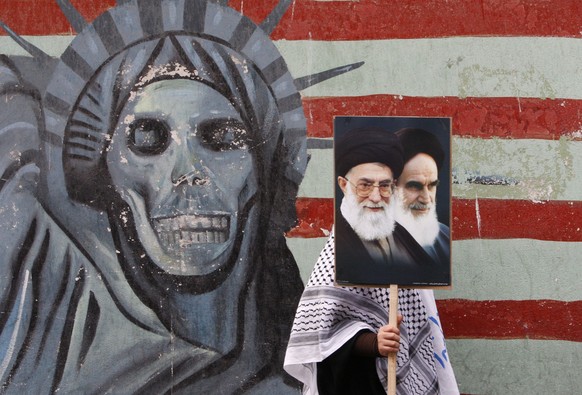 A pro-government Iranian female demonstrator, makes her way as she holds a poster showing pictures of the late revolutionary founder Ayatollah Khomeini, right, and supreme leader Ayatollah Ali Khamene ...