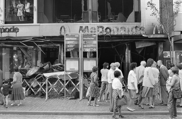 Passanten betrachten am fruehen Montagmorgen, 5. Juli 1982, den Schaden, den ein Grossbrand an einem zur amerikanischen MacDonalds-Kette gehoerendem Schnellimbiss-Restaurant in Zuerich verursacht hat. ...