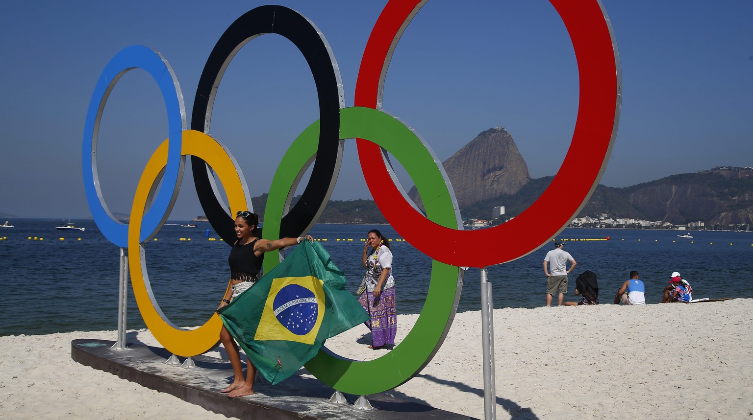 epa05493449 With temperatures reaching over 30 degrees is Rio de Janeiro specators at the viewing area on the beach of Guanabara Bay pose for pictures at the Olympic rings as they wait for wind during ...