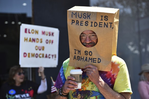 Jim Doxsee, of Pleasanton, wears a bag over his head as he marches with other protesters in Walnut Creek, Calif., on Saturday, March 29, 2025, during a demonstration against Elon Musk and the Presiden ...