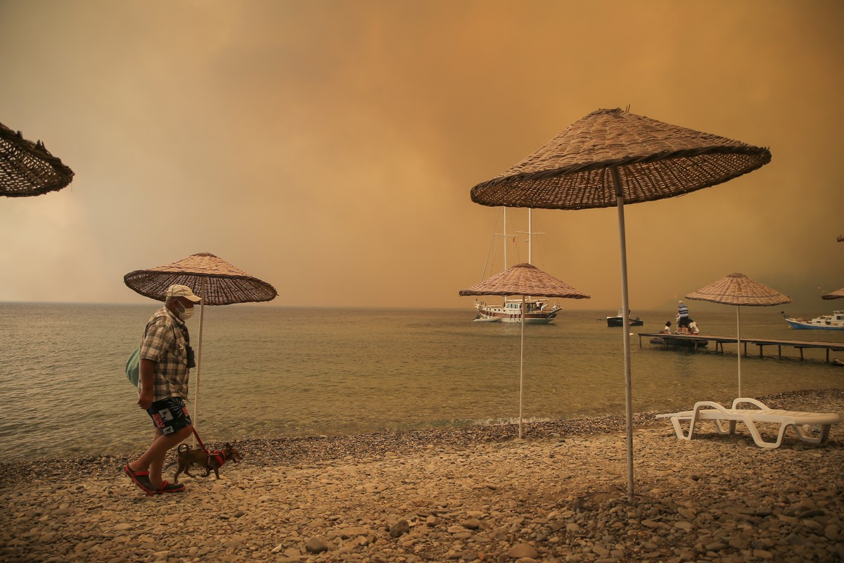 A man walks with his dog on the beach of smoke-engulfed Mazi area as wildfires rolled down the hill toward the seashore, in Bodrum, Mugla, Turkey, Sunday, Aug. 1, 2021. More than 100 wildfires have be ...